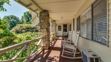 A covered porch with stone pillars, a wooden railing, and a white air conditioning unit.