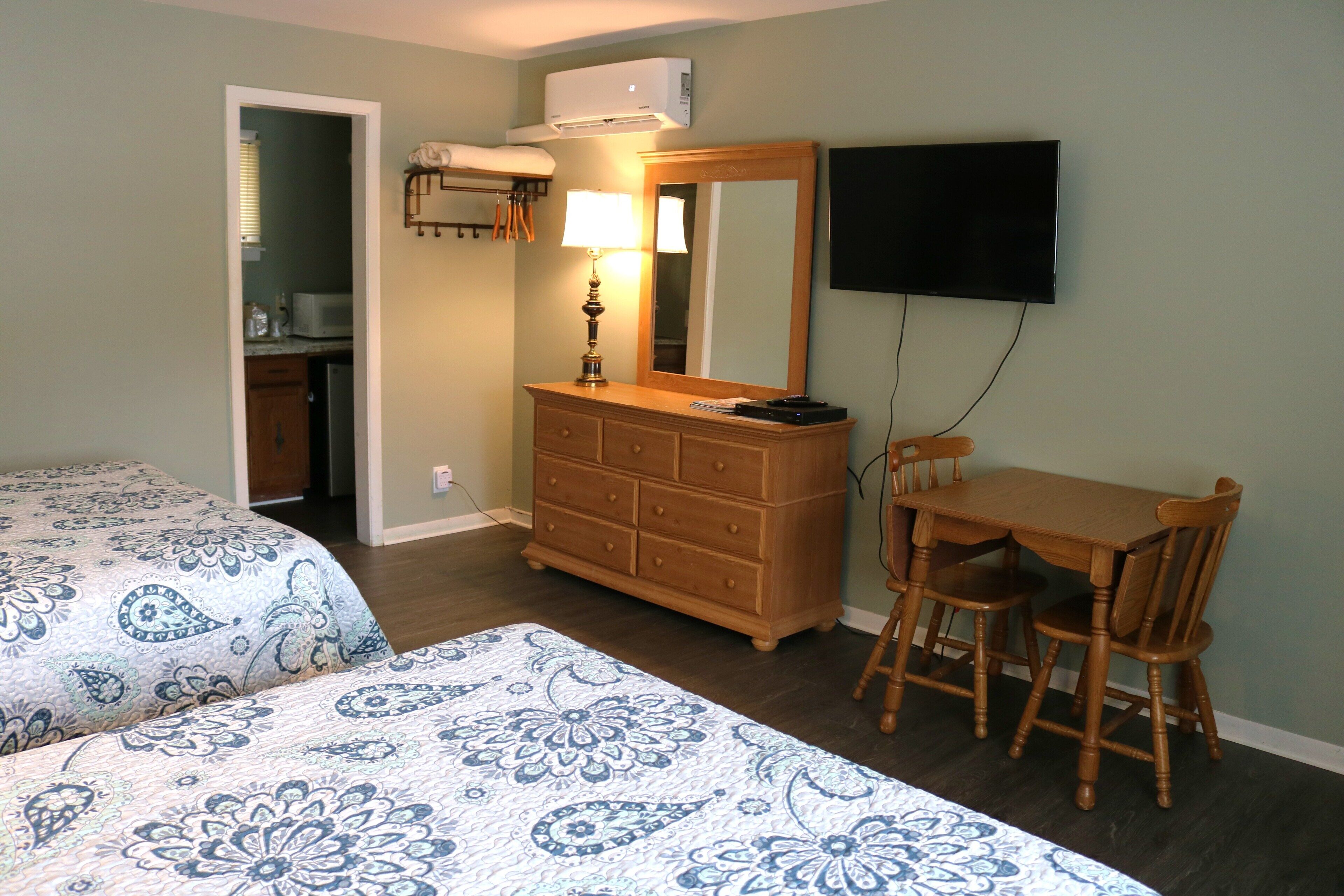 Slaapkamer met twee bedden, een dressoir, een bureau met stoel, een televisie en een airconditioner.