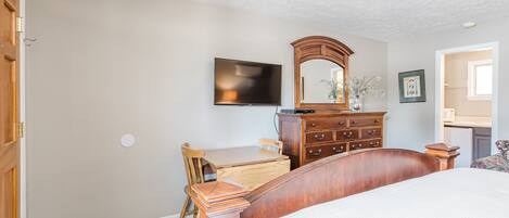 A bedroom with a bed, a wooden dresser, a desk, a chair, a television, and a mirror.