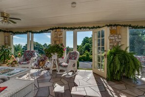 A covered patio with wicker furniture, potted plants, and a view of the outdoors.