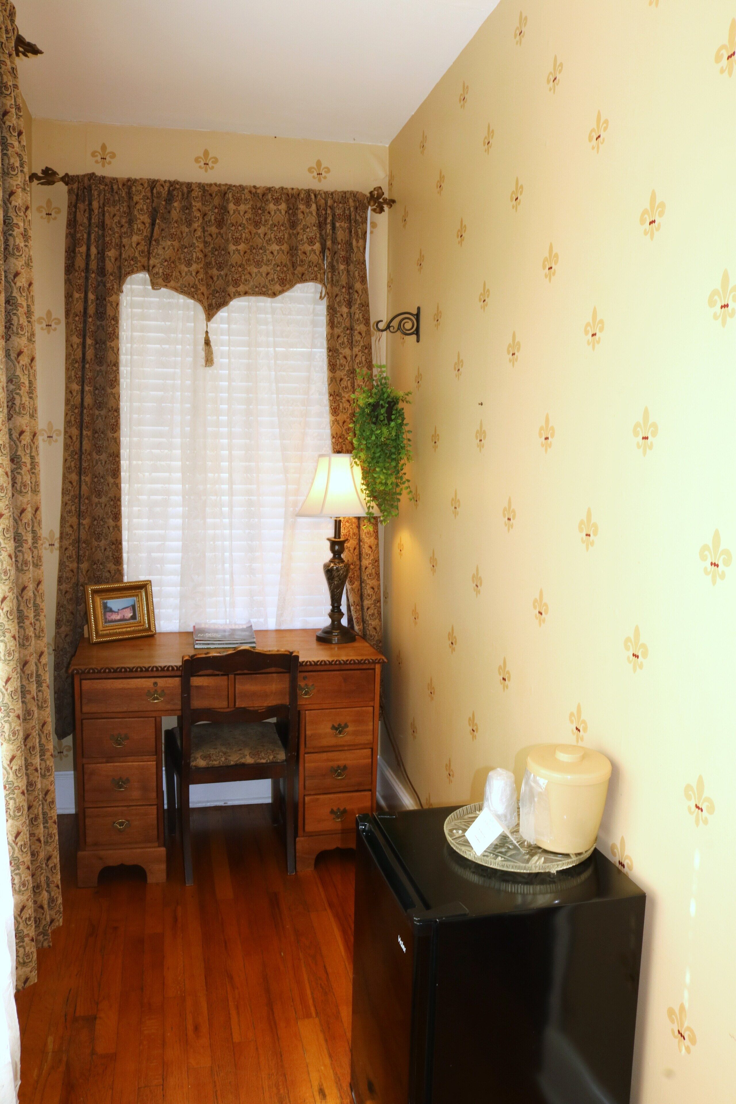 A room with a wooden desk, a chair, a lamp, a radiator, and a wall with floral wallpaper.