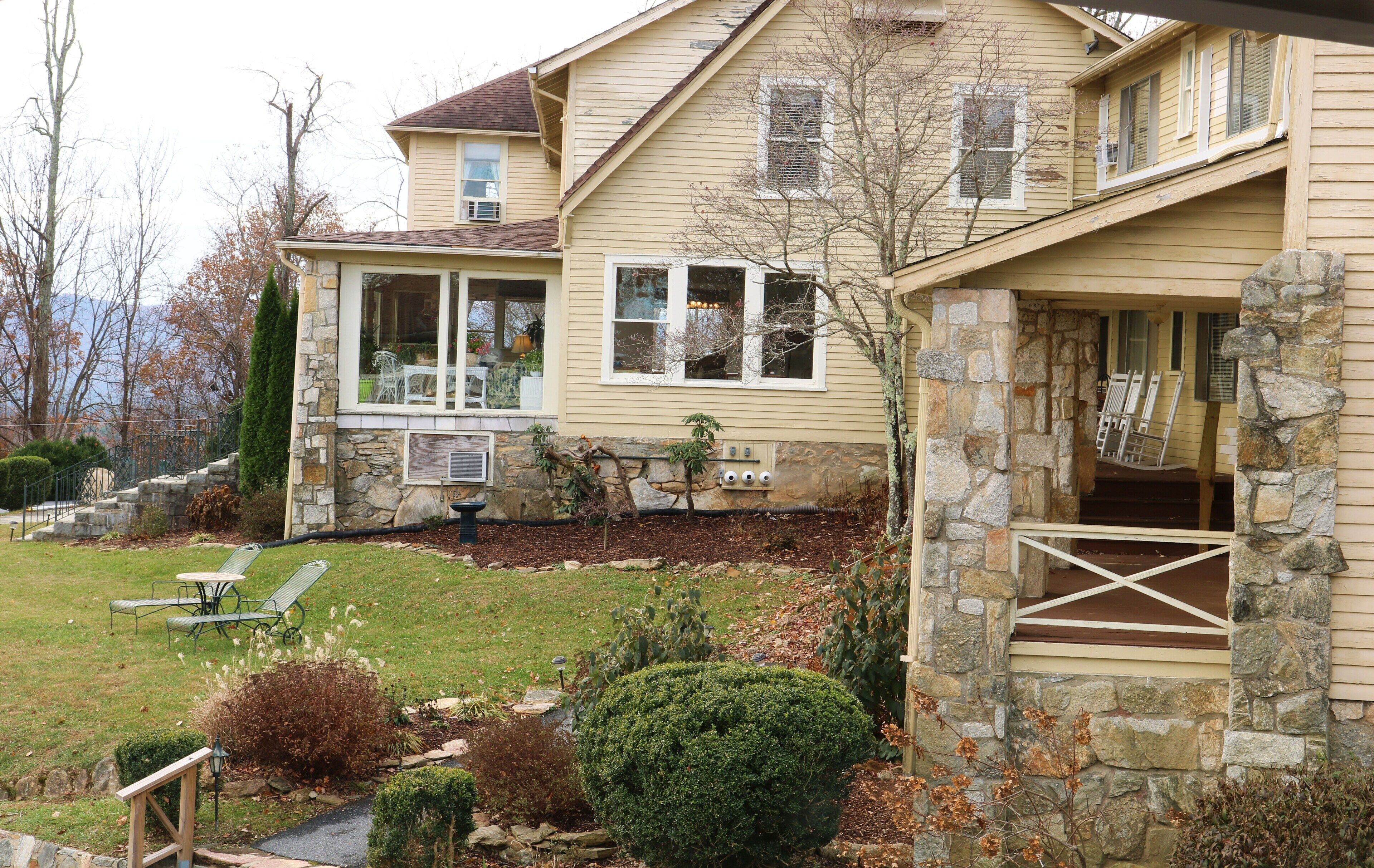 A two-story house with a stone porch, a covered front porch, and a lawn with outdoor furniture.