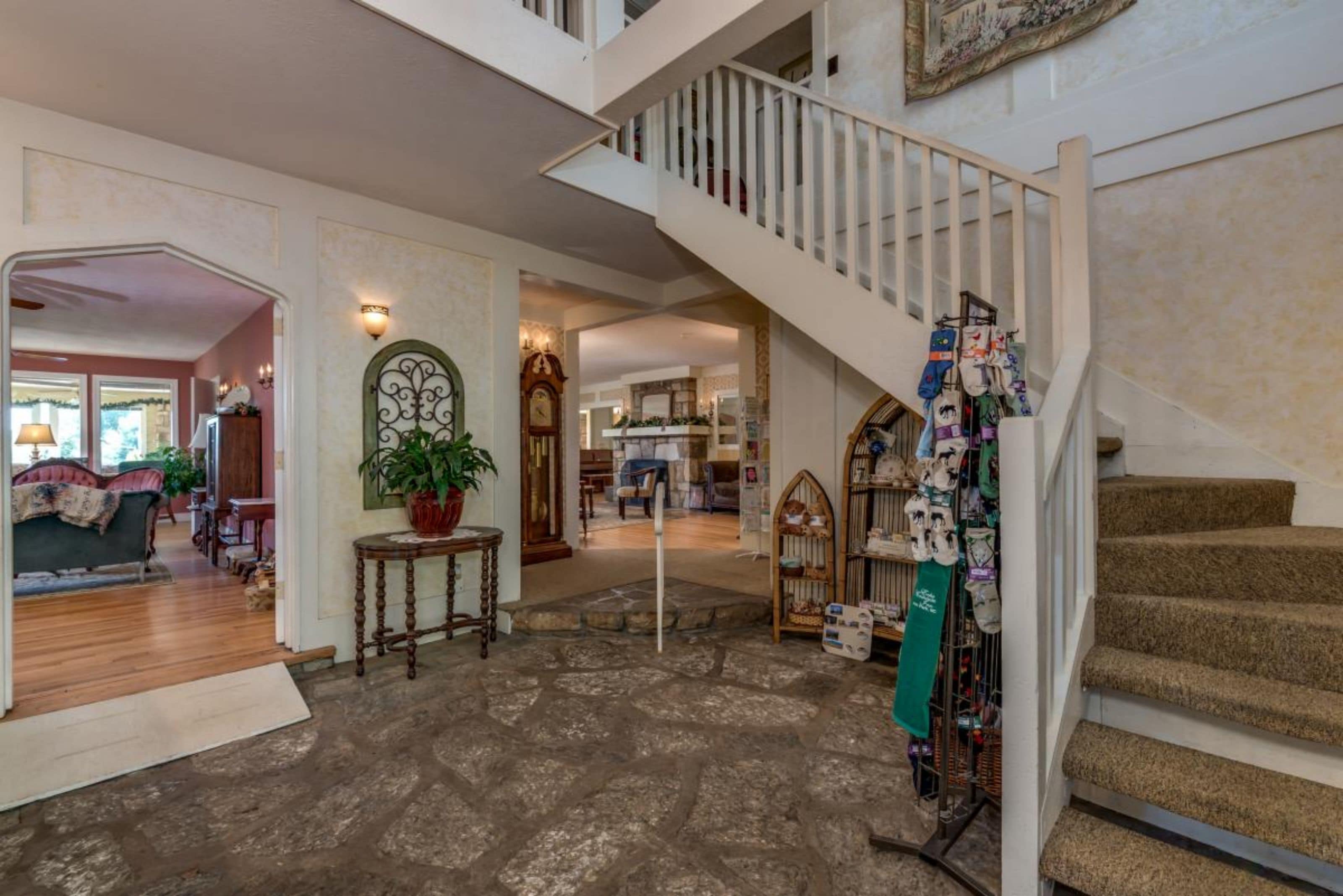 A spacious foyer with a stone floor, a staircase with a white railing, and a display of various items on the lower level.