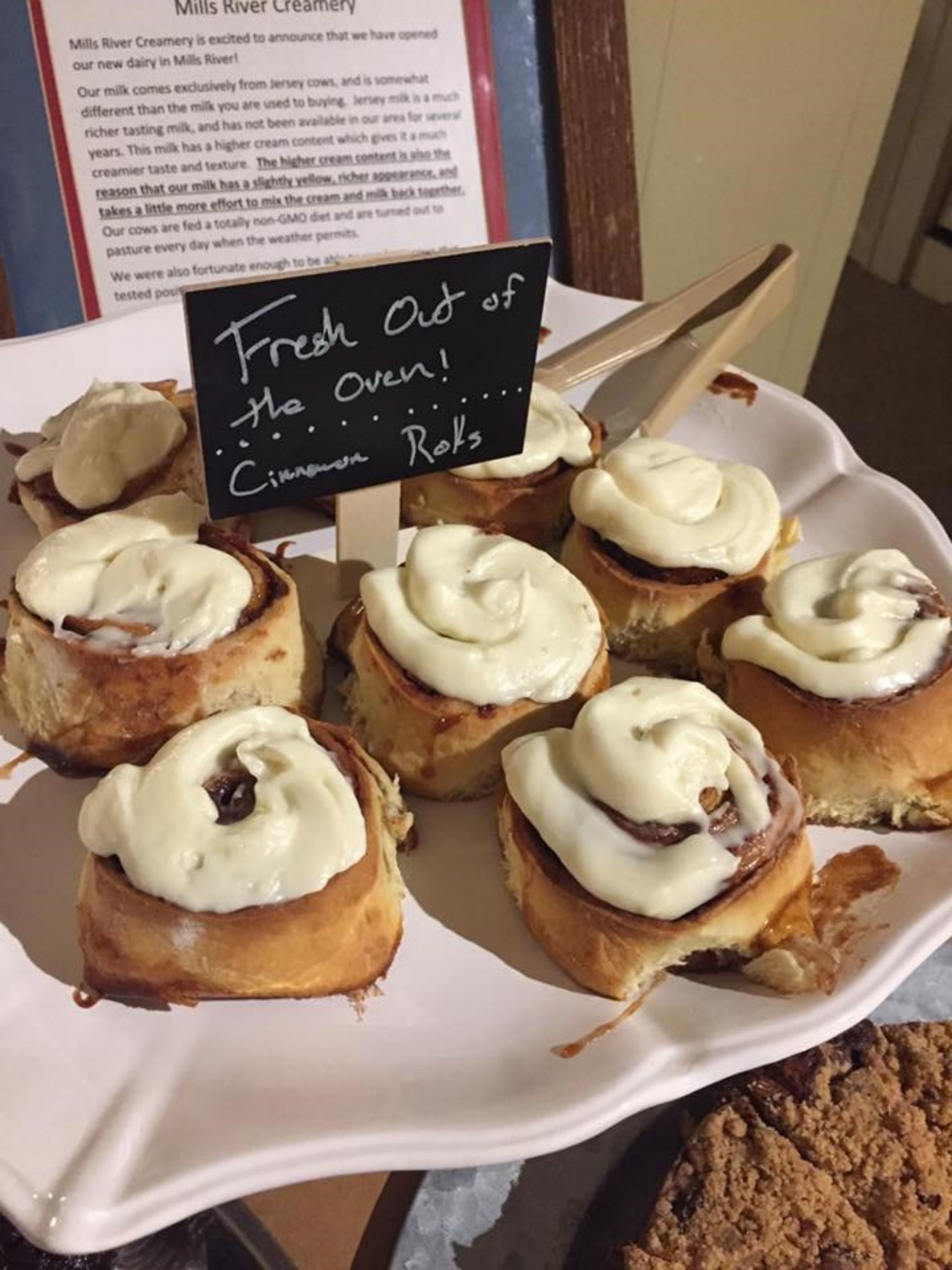 Une assiette de brioches à la cannelle recouvertes d’un glaçage blanc, avec une étiquette indiquant qu’elles viennent tout juste de sortir du four.