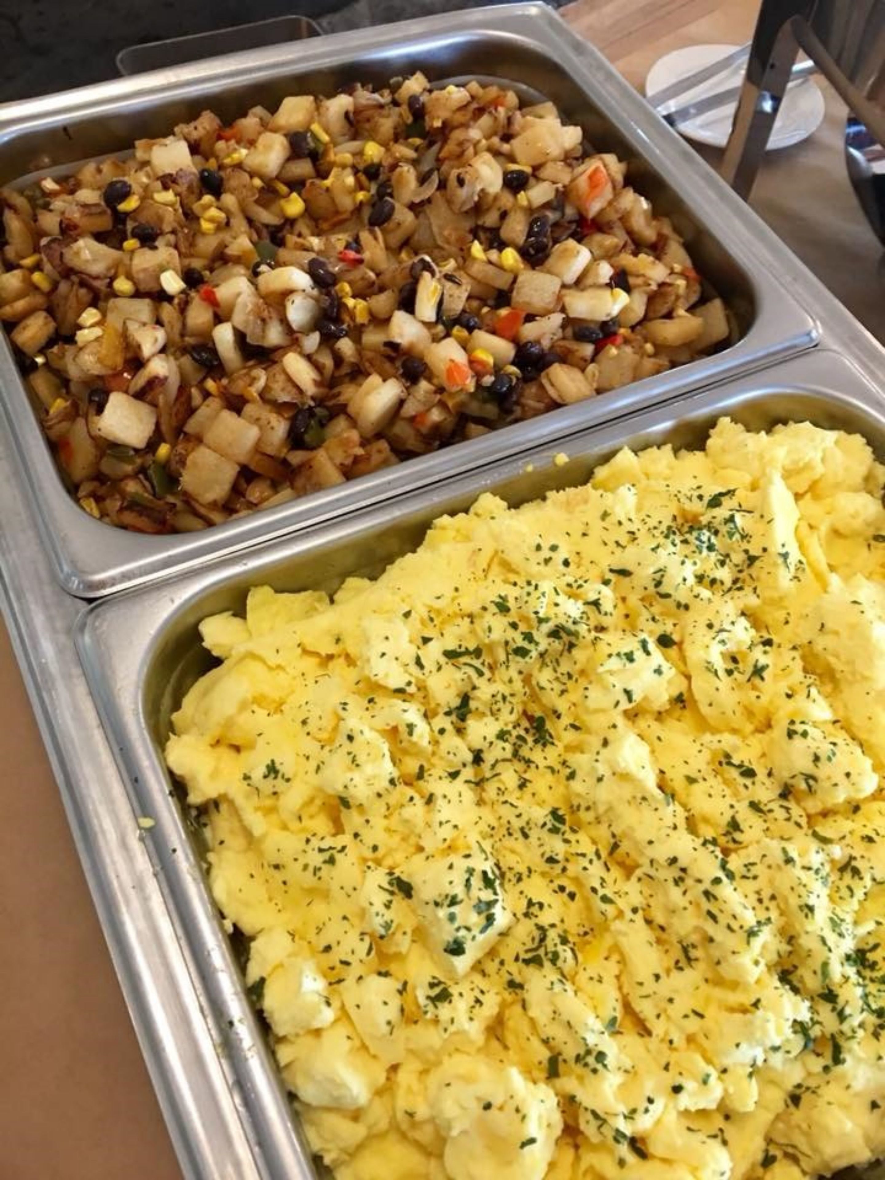 Un buffet proposant deux plateaux de nourriture : l’un contenant un plat de légumes et de haricots, et l’autre, une purée de pommes de terre garnie d’herbes.