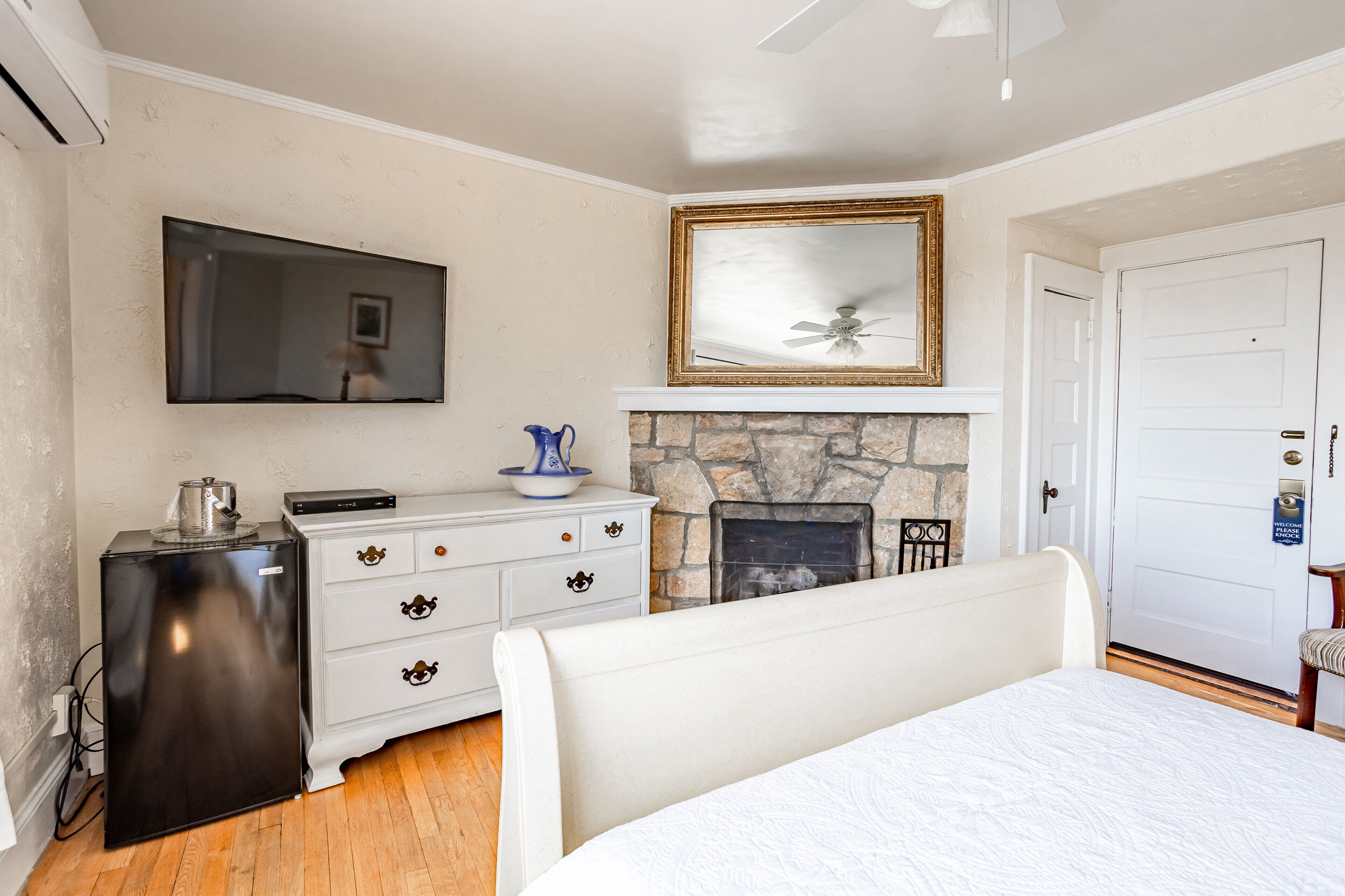 A bedroom with a bed, a dresser, a television, a fireplace, and a door with a sign.