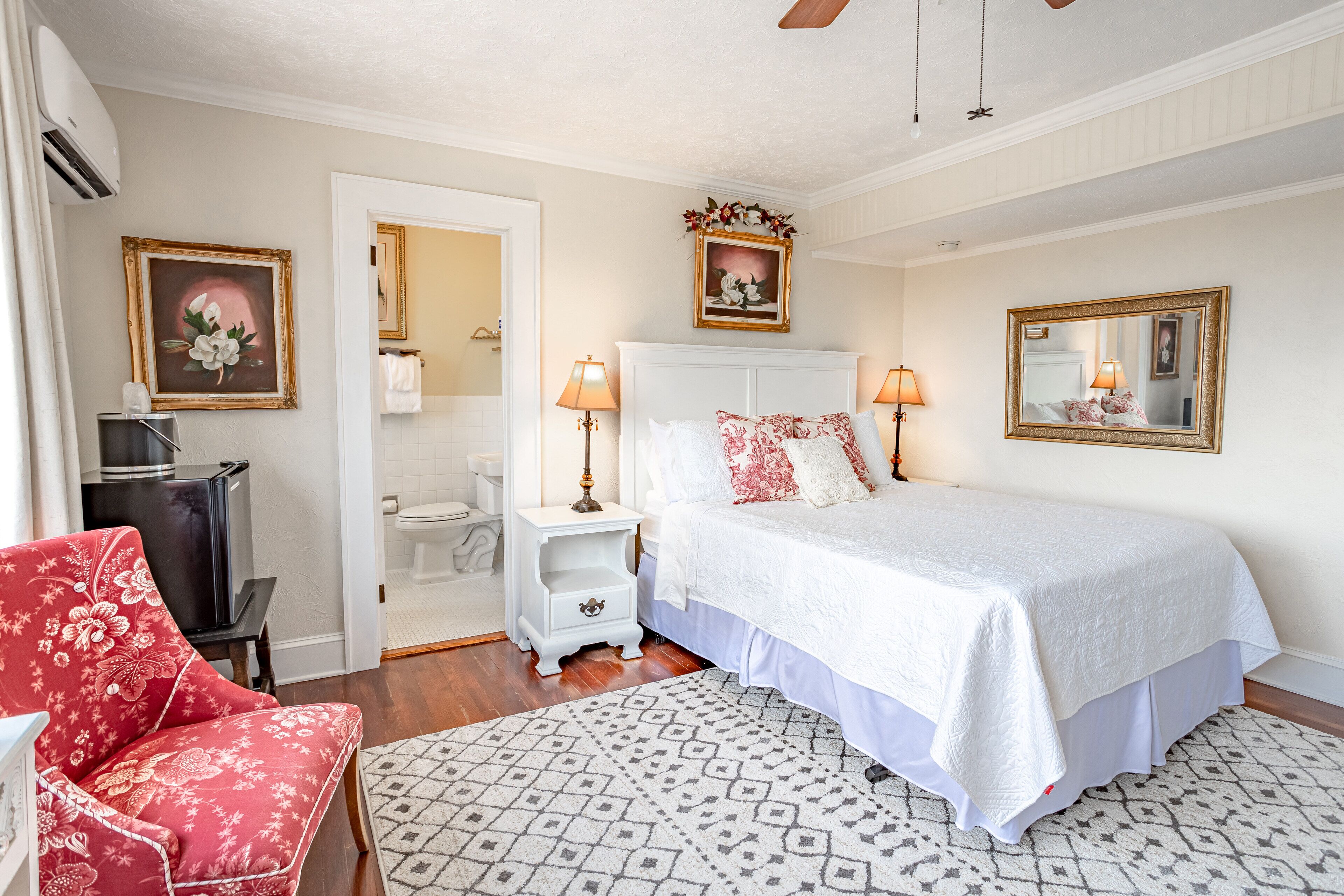 A bedroom with a bed, bedside lamps, a nightstand, a chair, and a mirror.
