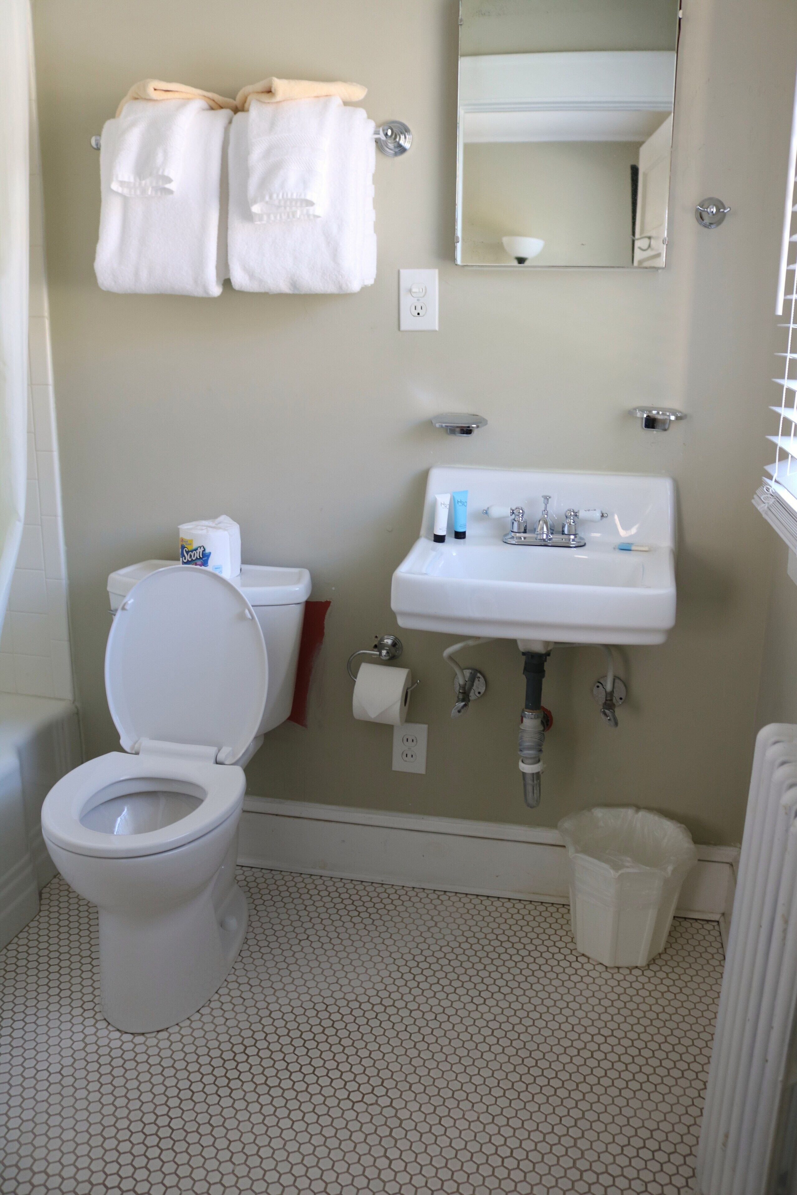 A bathroom with a toilet, sink, mirror, and two towels hanging on the wall.