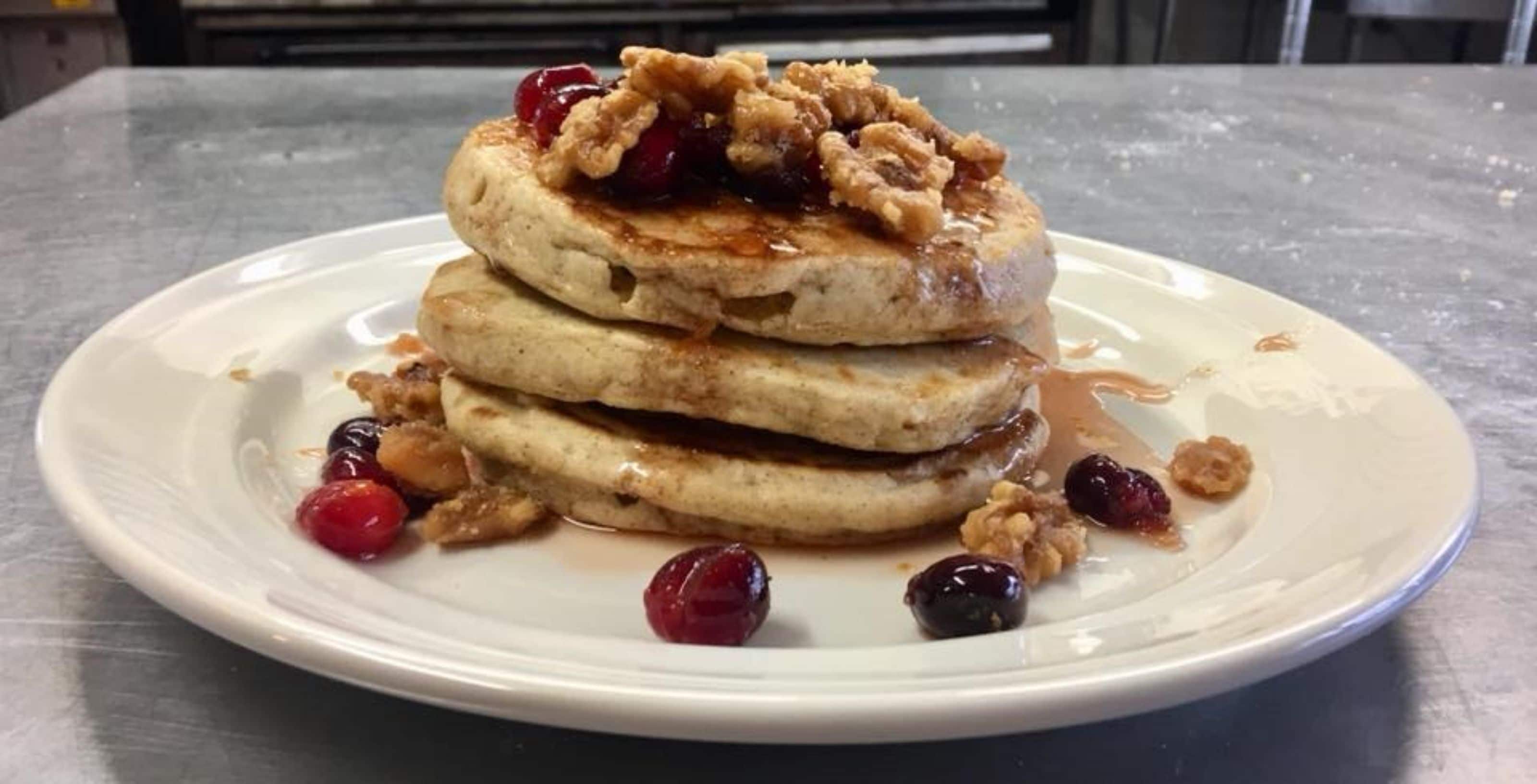 Una pila di pancake su un piatto bianco con sciroppo e frutti di bosco.
