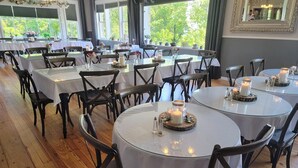 Un restaurant avec des tables rondes recouvertes de nappes blanches, des chaises en bois foncé et des bougies posées sur des sous-verres.