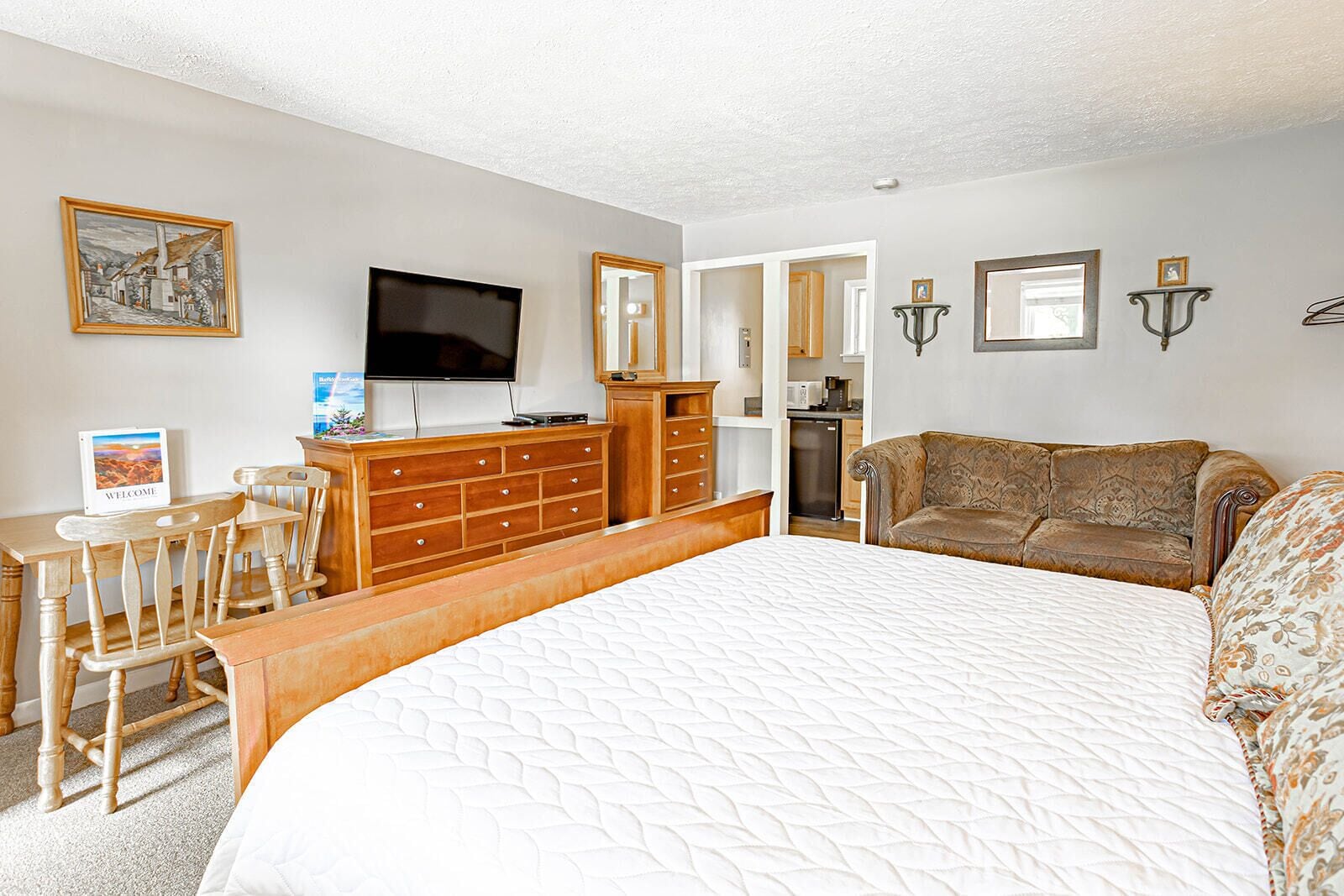 A bedroom with a large bed, wooden dresser, TV, and a sofa.
