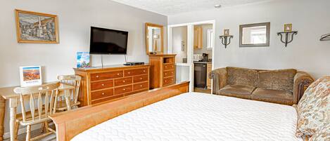 A bedroom with a large bed, wooden dresser, TV, and a sofa.