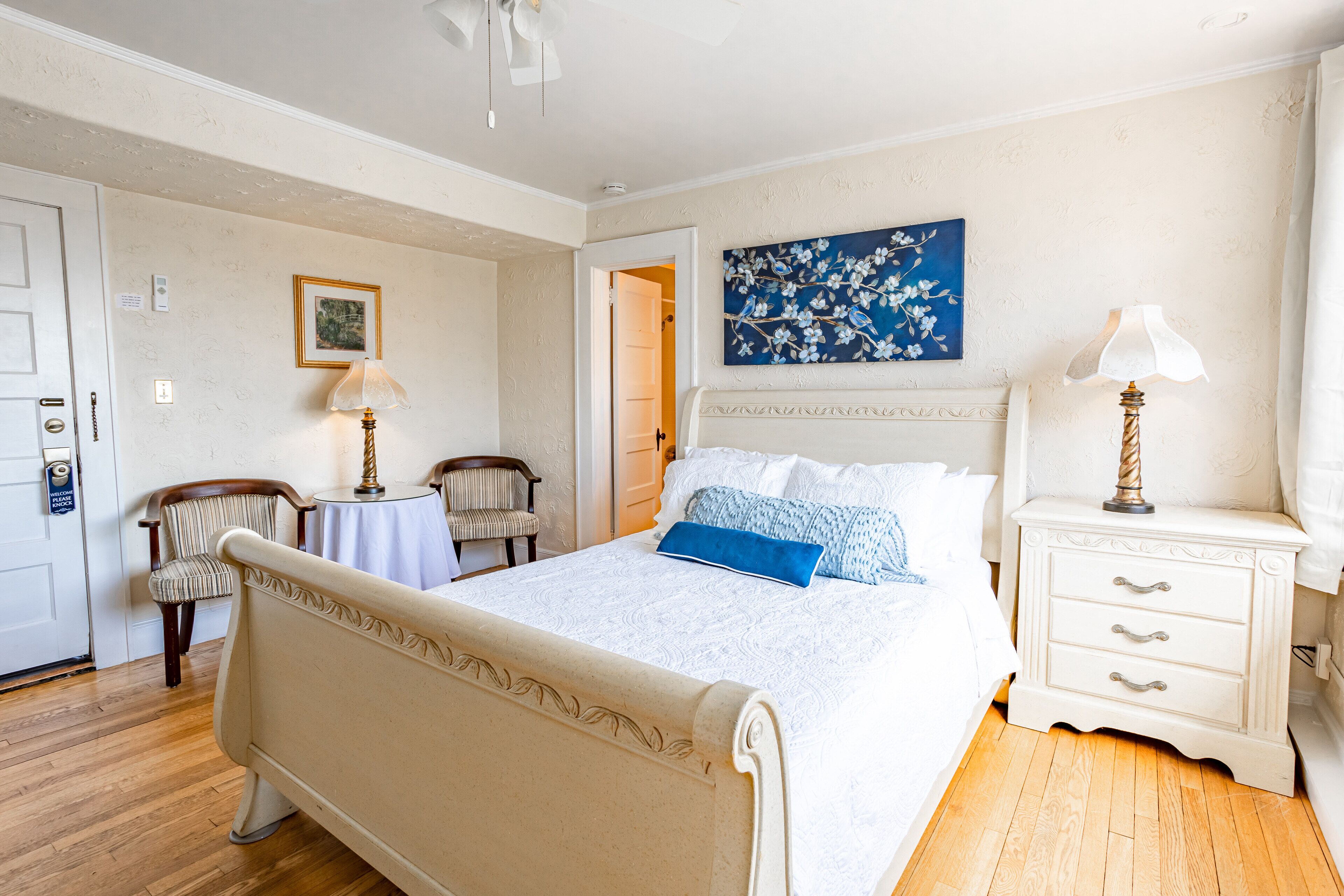 A neatly arranged bedroom with a bed, bedside tables, a chair, and a painting on the wall.