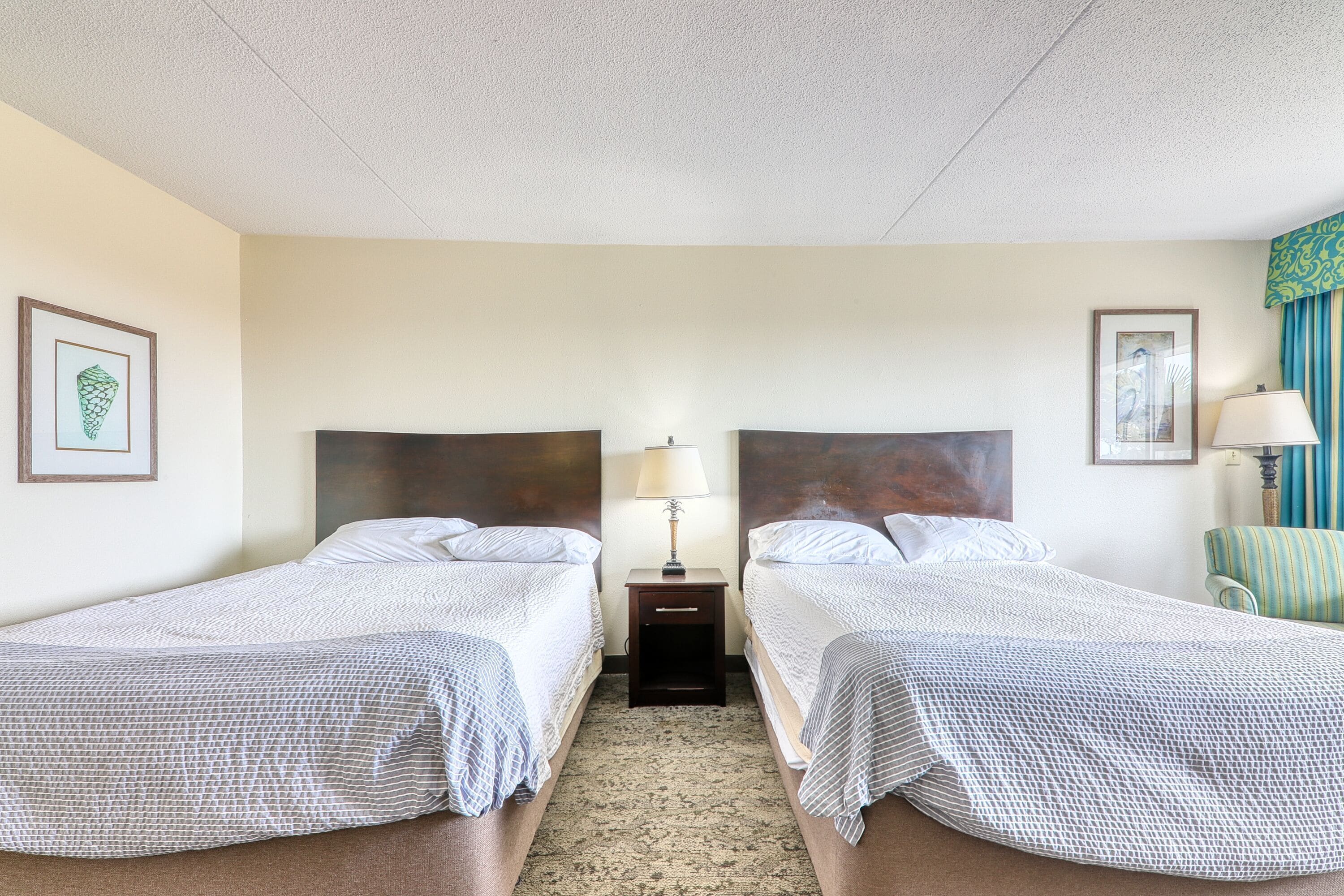Une chambre d’hôtel avec deux lits, une table de chevet avec une lampe et une chaise.