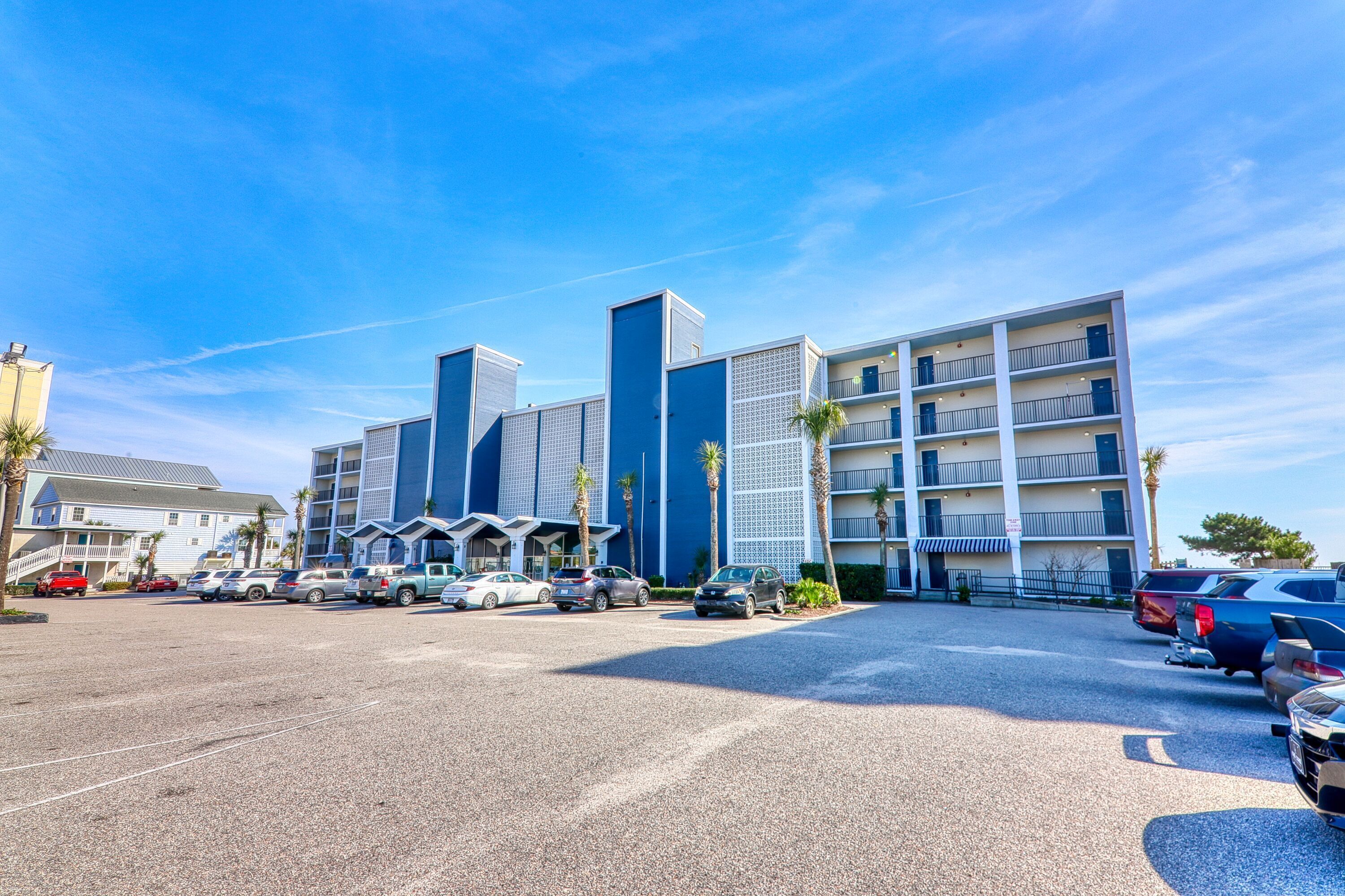 Un hôtel moderne à plusieurs étages, doté d’un parking et où plusieurs voitures sont garées devant.