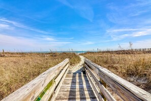 A wooden boardwalk leading to a beach with a clear sky.