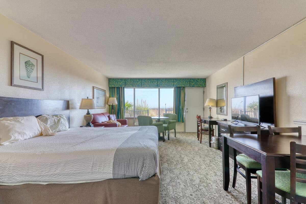 A hotel room with a large bed, a desk with a chair, a television, and a window with curtains.