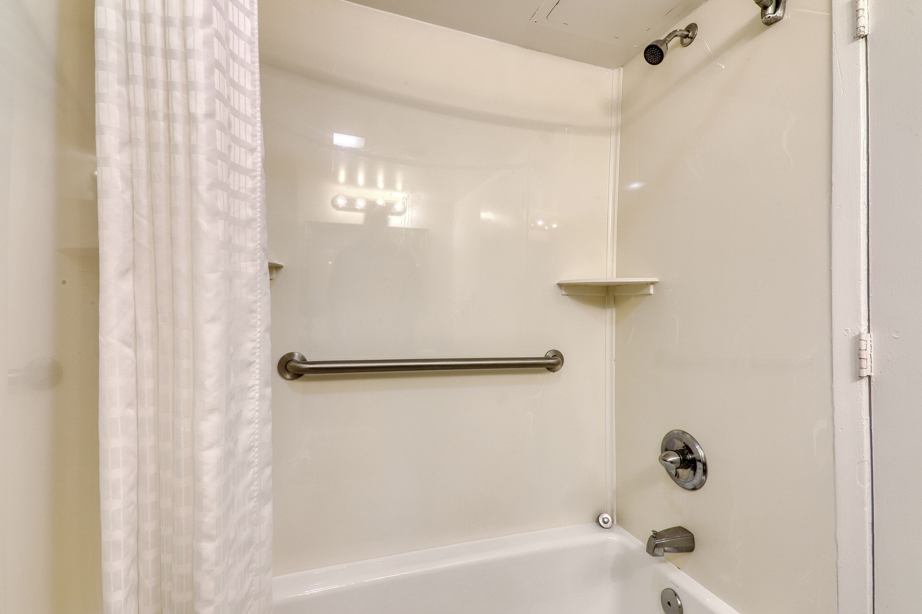 A white shower with a glass door, a grab bar, and a handheld showerhead.