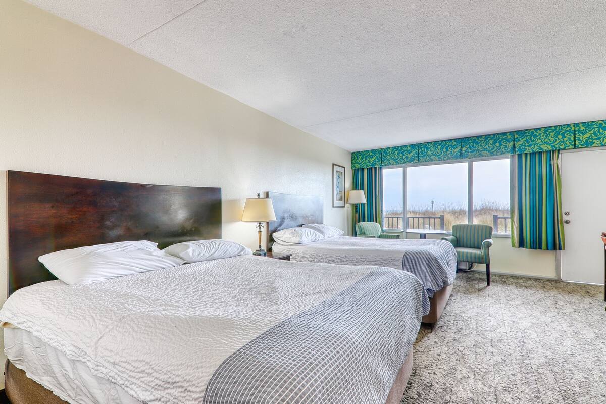A hotel room with two beds, a large window with curtains, a chair, and a view of the outside.