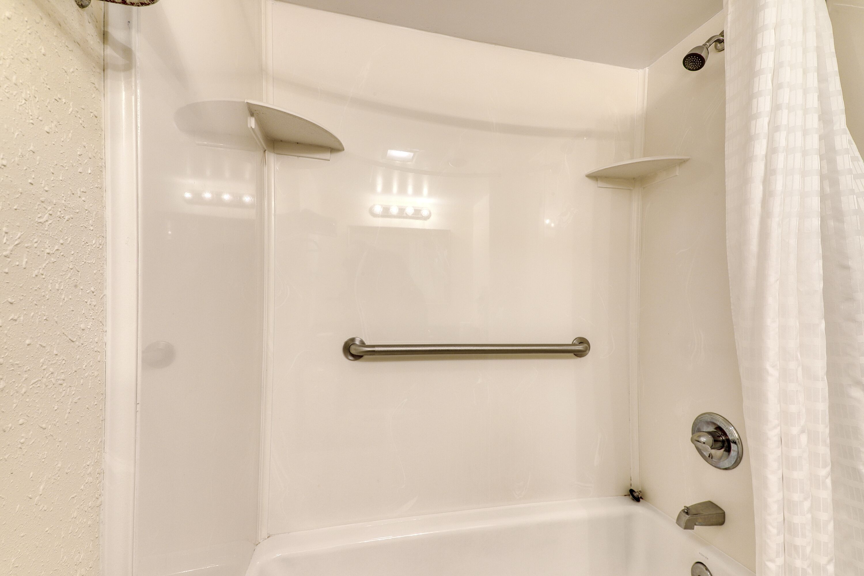 A bathroom with a bathtub, a shower, and a handrail.