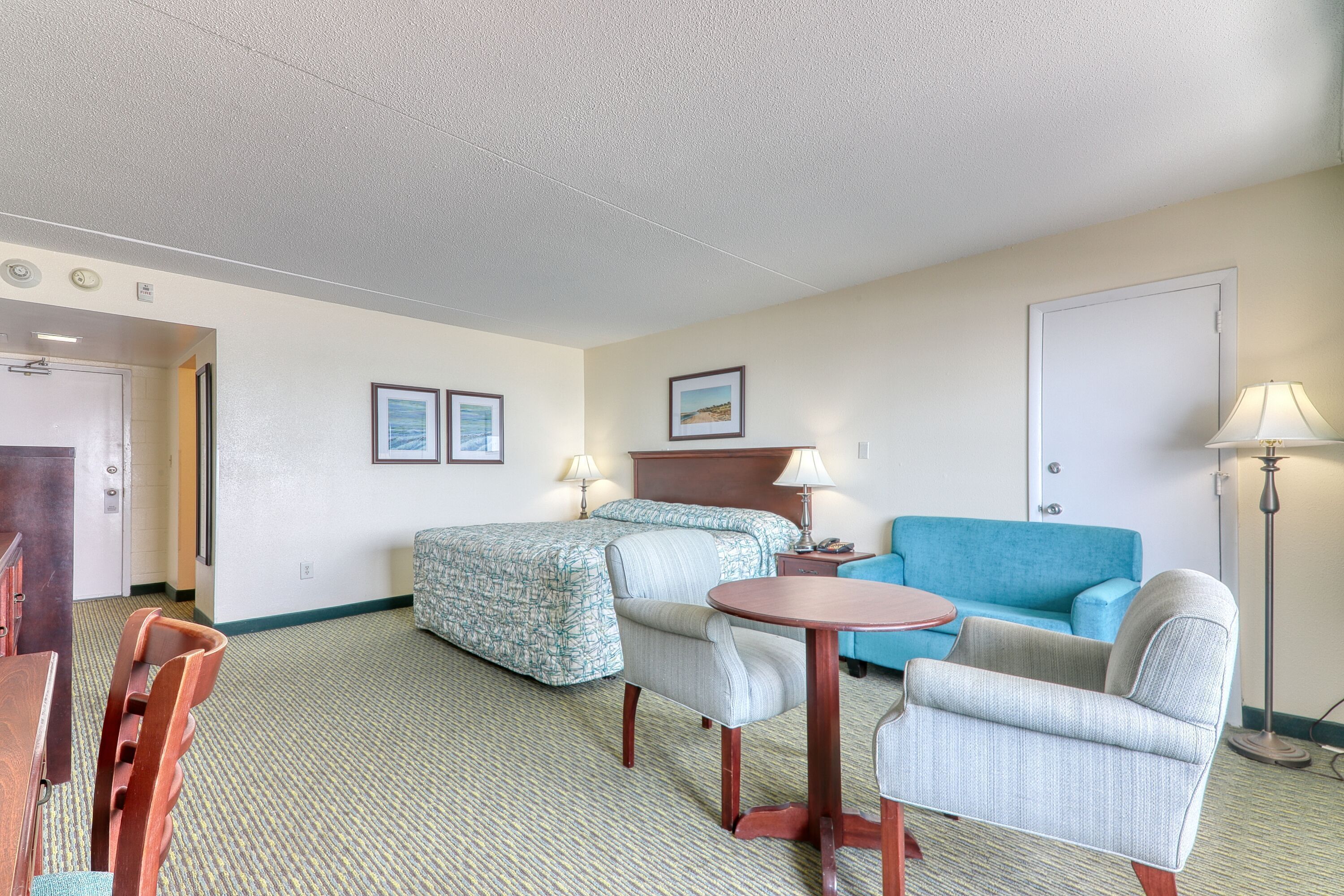 A hotel room with a bed, two chairs, a small table, a blue sofa, and a lamp.