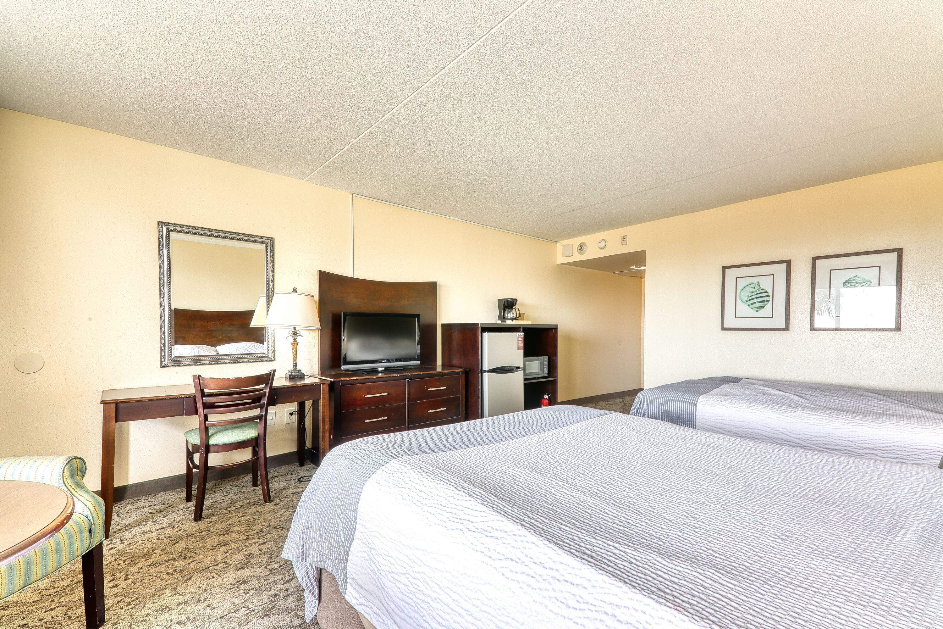 A hotel room with two beds, a desk with a chair, a television, a refrigerator, and two framed pictures on the wall.