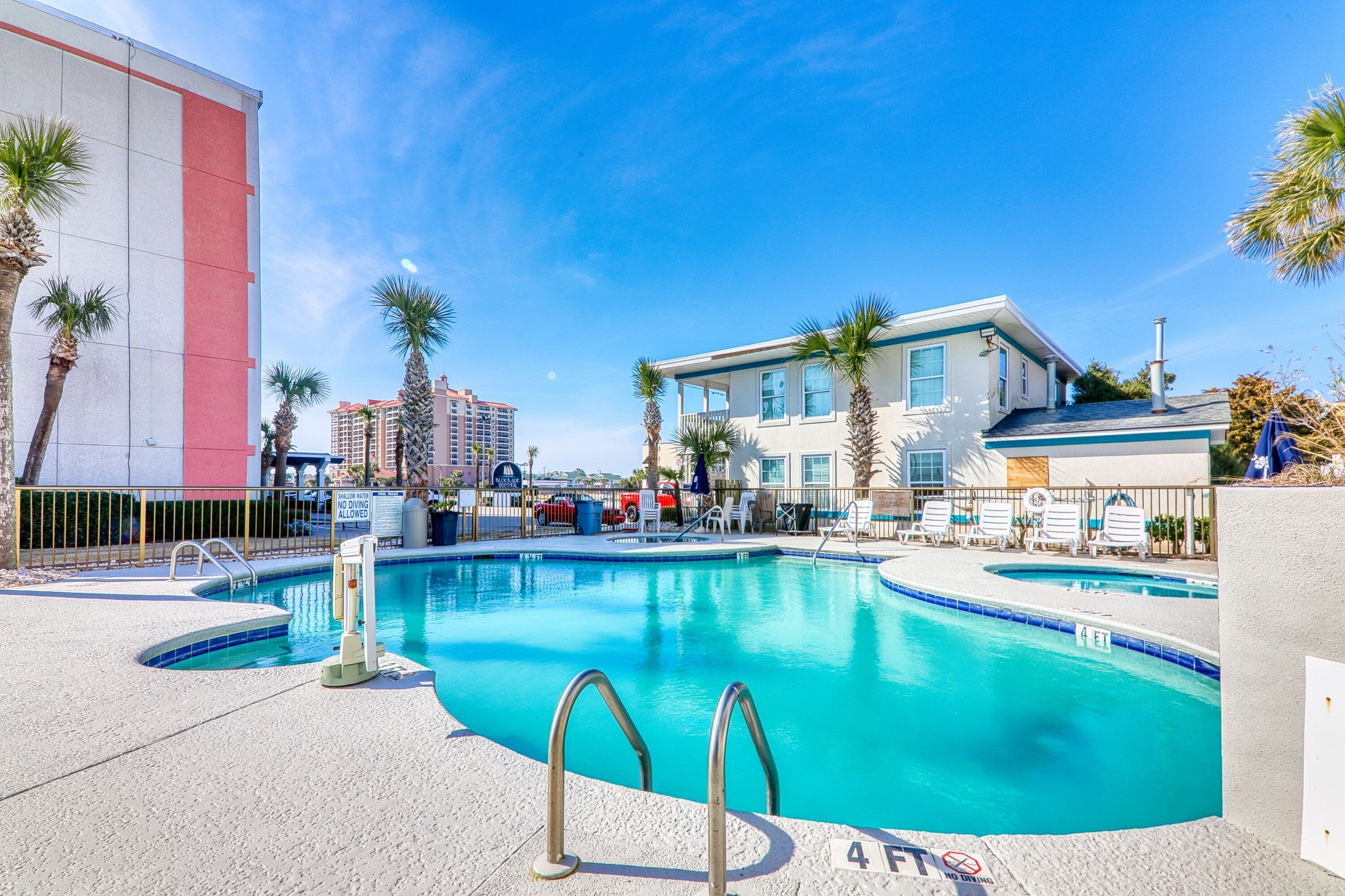 A swimming pool with a 4ft depth marker, surrounded by palm trees and a building with a red and white facade.