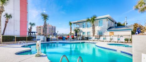 A swimming pool with a 4ft depth marker, surrounded by palm trees and a building with a red and white facade.