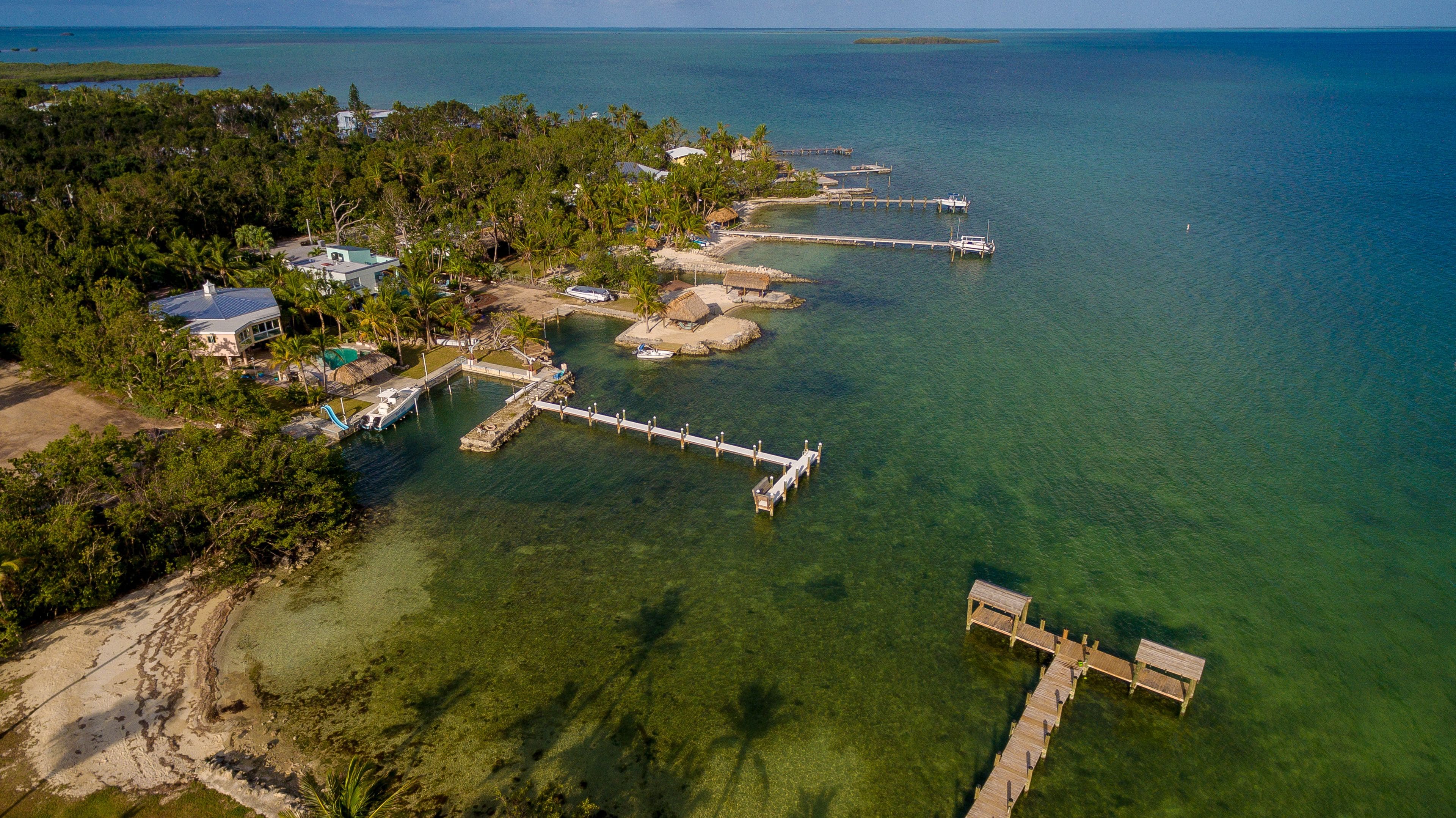 An aerial view of a coastal property with clear waters, a dock, and a house with a swimming pool.