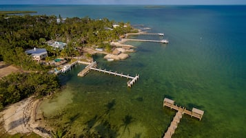 An aerial view of a coastal property with clear waters, a dock, and a house with a swimming pool.
