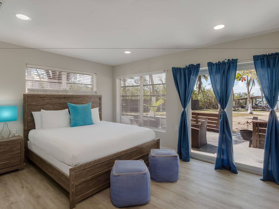 A bedroom with a wooden bed, a nightstand, a lamp, and a view of the outdoors through large windows.