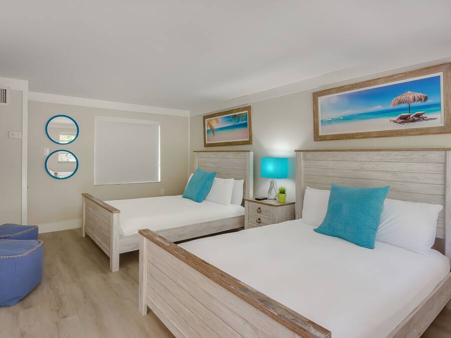 A hotel room with two beds, a TV, a painting of a beach, and a small table with a lamp.
