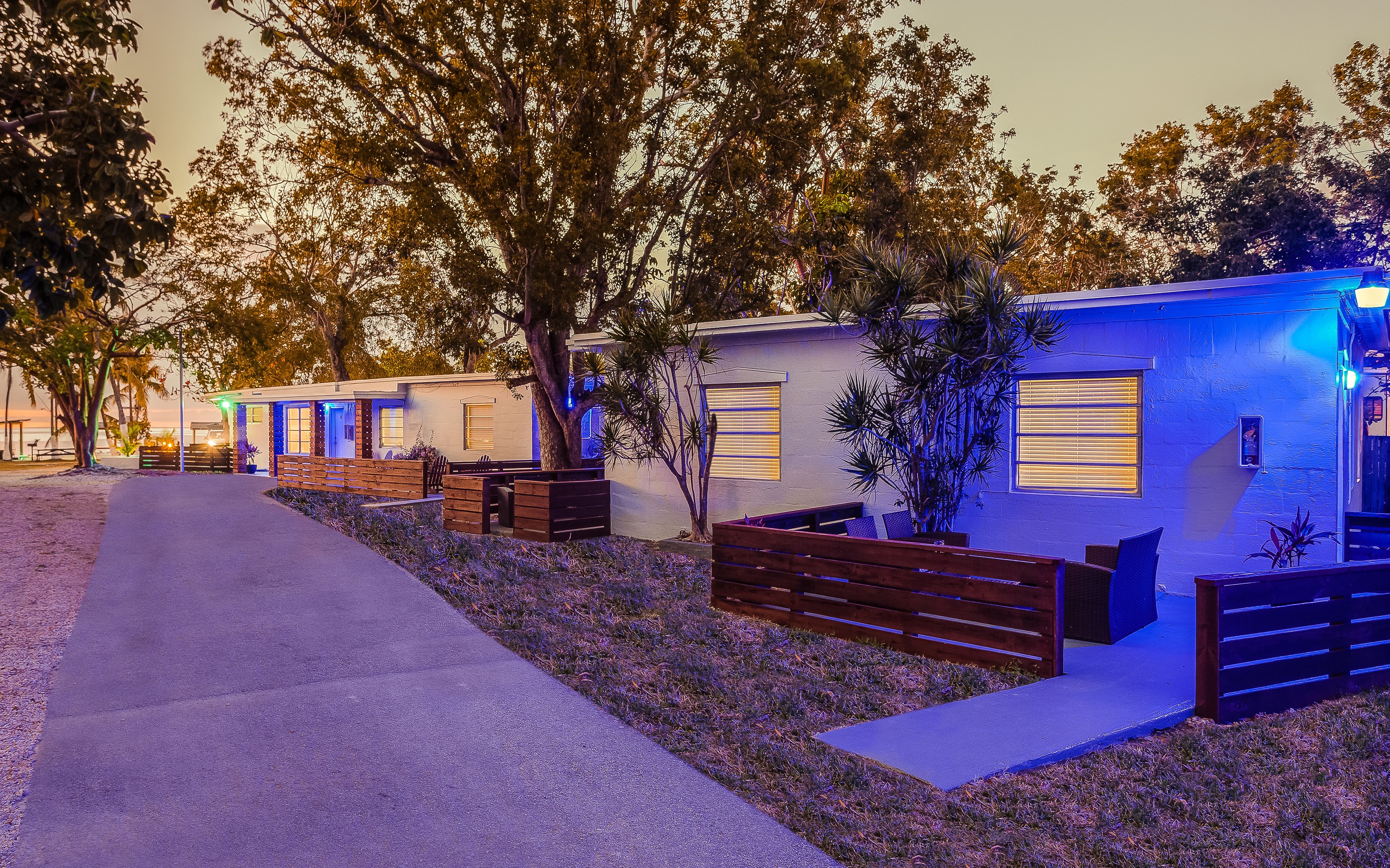 A row of compact, single-story cabins with individual windows and outdoor seating areas, surrounded by trees and a paved walkway.