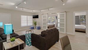 A modern living room with a sofa, a glass coffee table, a TV, and a sliding door leading to a bedroom. - Drift Hotel (Key Largo)