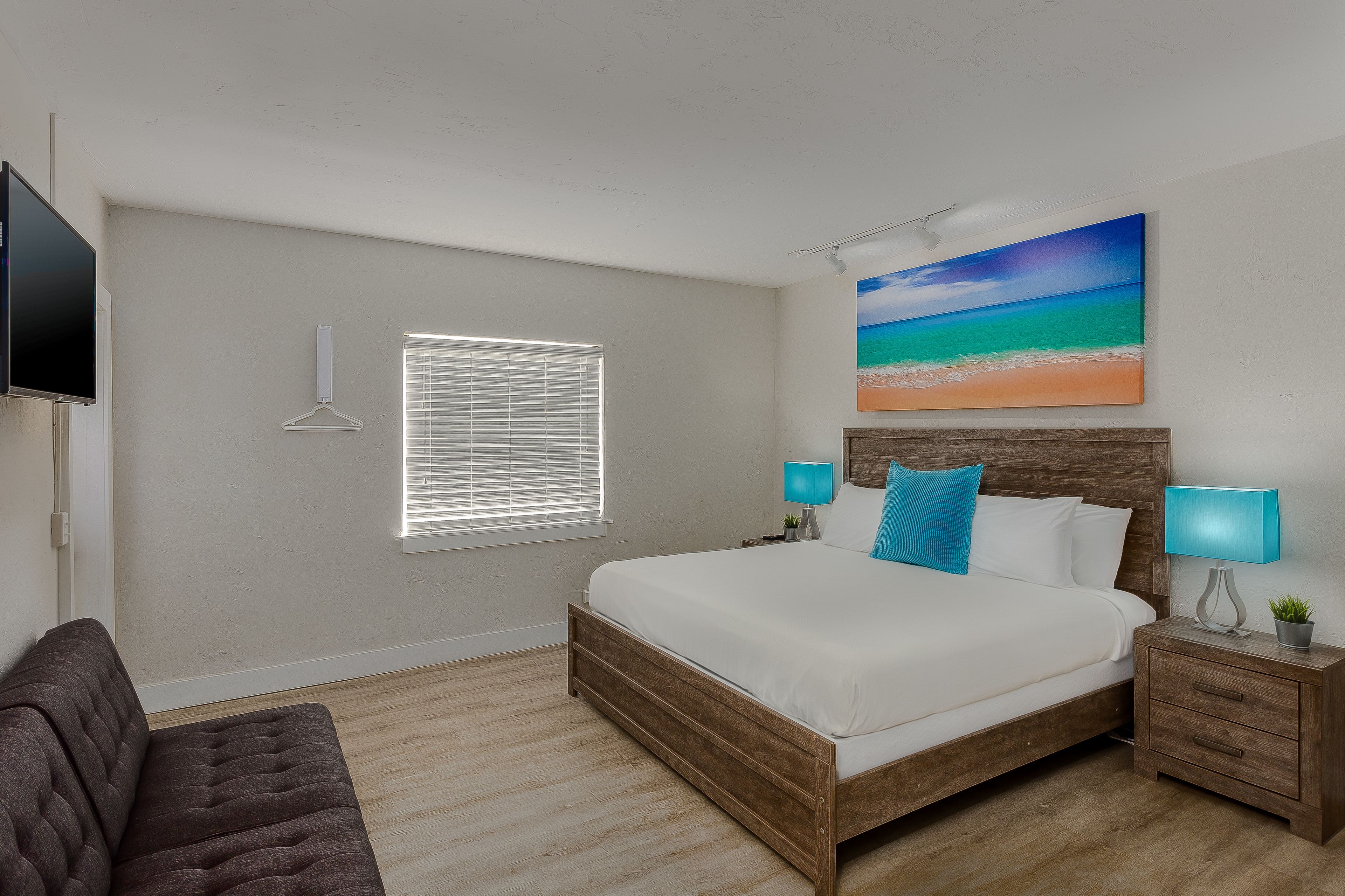 A bedroom with a bed, bedside tables, a TV, and a window with blinds.
