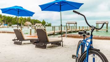 A beach with lounge chairs and blue umbrellas, a bicycle, and a wooden pier extending into the water.