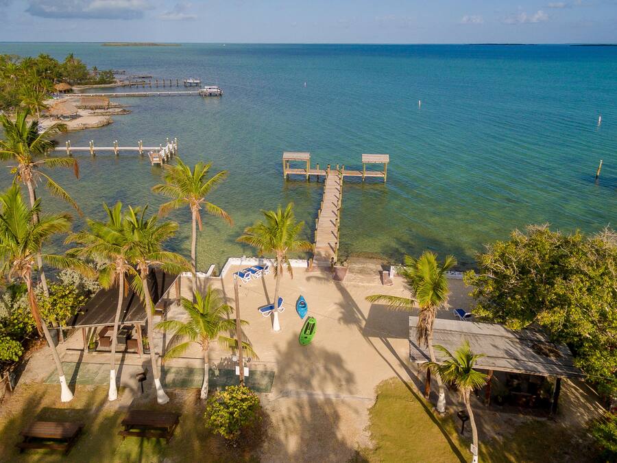 Un resort en la playa con muelle, palmeras y agua azul cristalina.