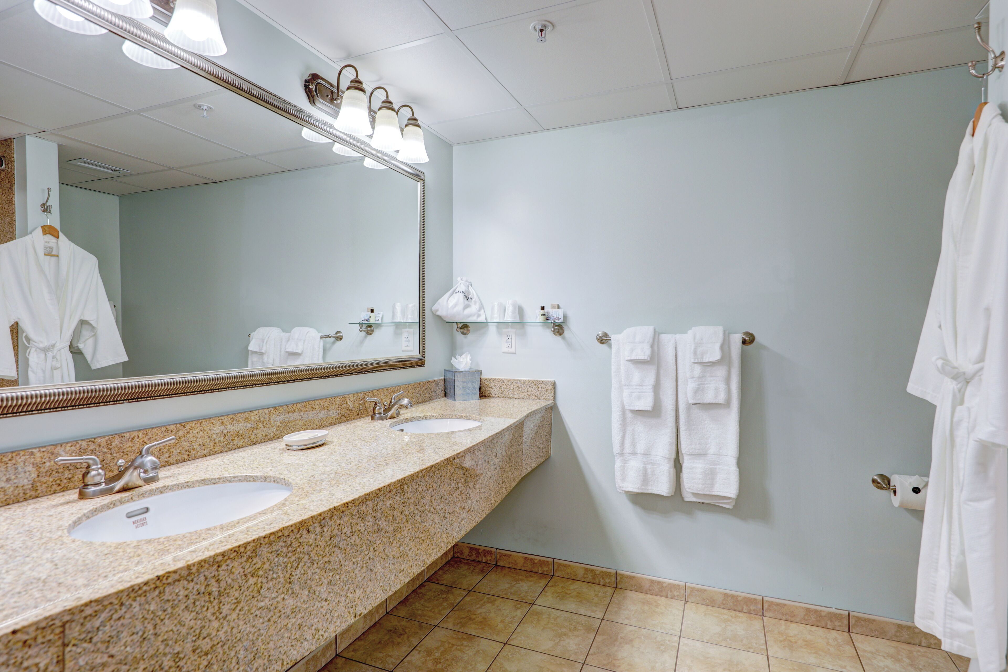 A bathroom with two sinks, a large mirror, and towels on the wall.