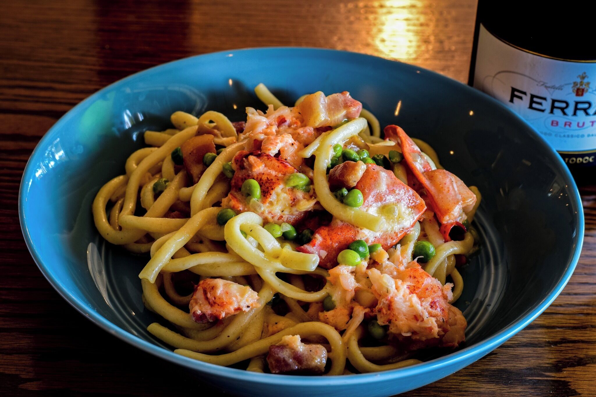 A bowl of pasta with shrimp and peas, and a bottle of wine in the background.