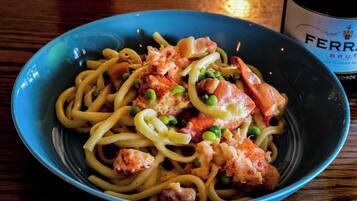 A bowl of pasta with shrimp and peas, and a bottle of wine in the background.