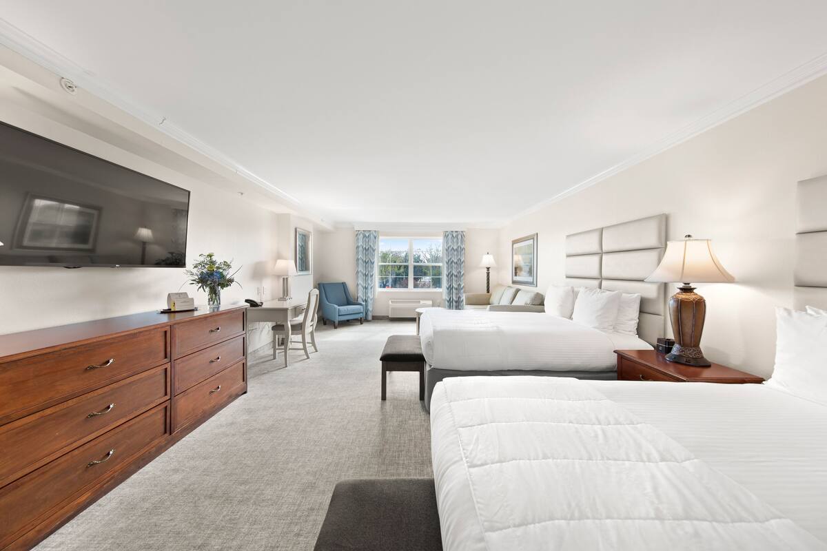 A hotel room with a large bed, a desk with a chair, a dresser, and a television on the wall.