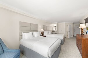 Una habitación de hotel con dos camas, una silla azul, un aparador de madera y un espejo.