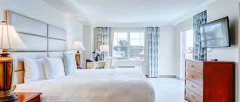 A hotel room with a large bed, bedside lamps, a dresser, a television, and a window with curtains.