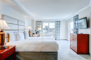 A hotel room with a large bed, bedside lamps, a dresser, a television, and a window with curtains.