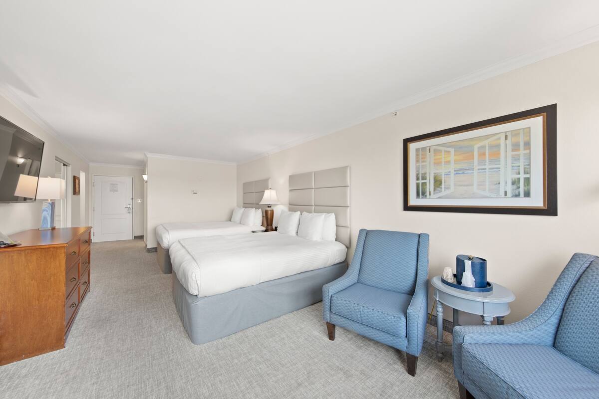 A hotel room with a bed, two chairs, a small table, and a dresser.