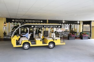 A yellow golf cart with a sign reading "HOTEL REHOBOTH" parked in front of a building with a similar sign.