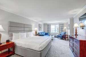 A hotel room with a large bed, a sofa, a chair, a dresser, and a window with curtains.