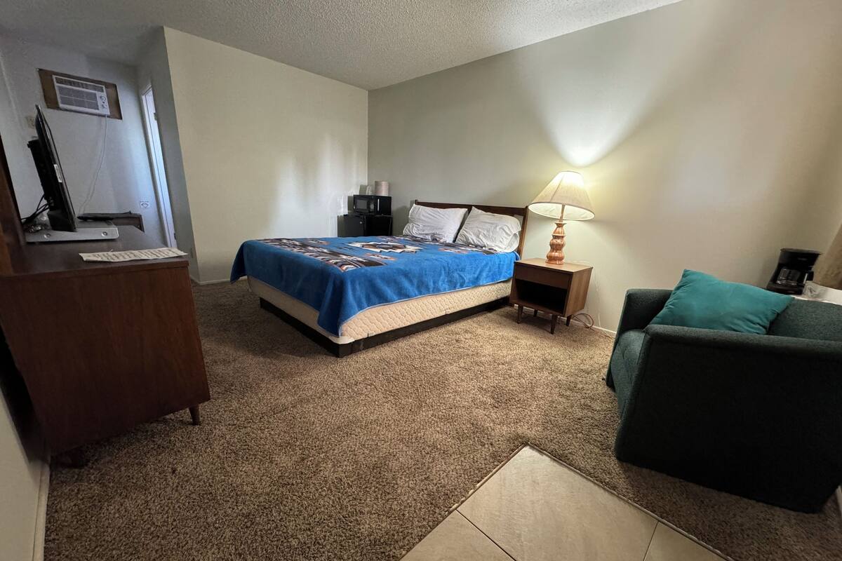 A bedroom with a bed, a desk, a chair, a nightstand, and a lamp.