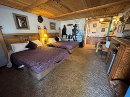 A cozy room with two beds, a wooden ceiling, and a kitchenette area.