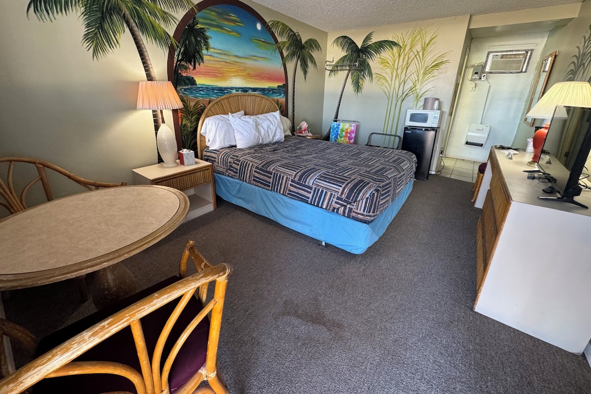 A hotel room with a bed, a desk, a chair, a table, and a wall mural.